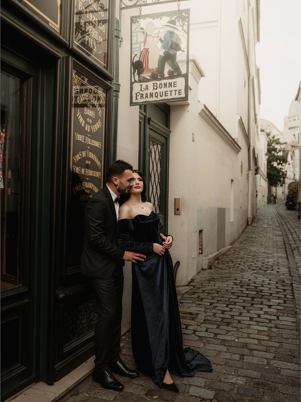 A couple standing close together in the doorway of an old Montmartre restaurant, the empty street running away behind them