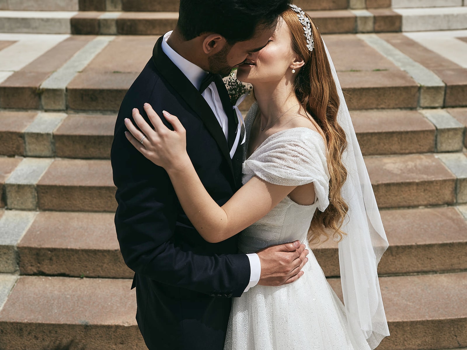 A bride resting a hand on her husband’s chest on a stone staircase
