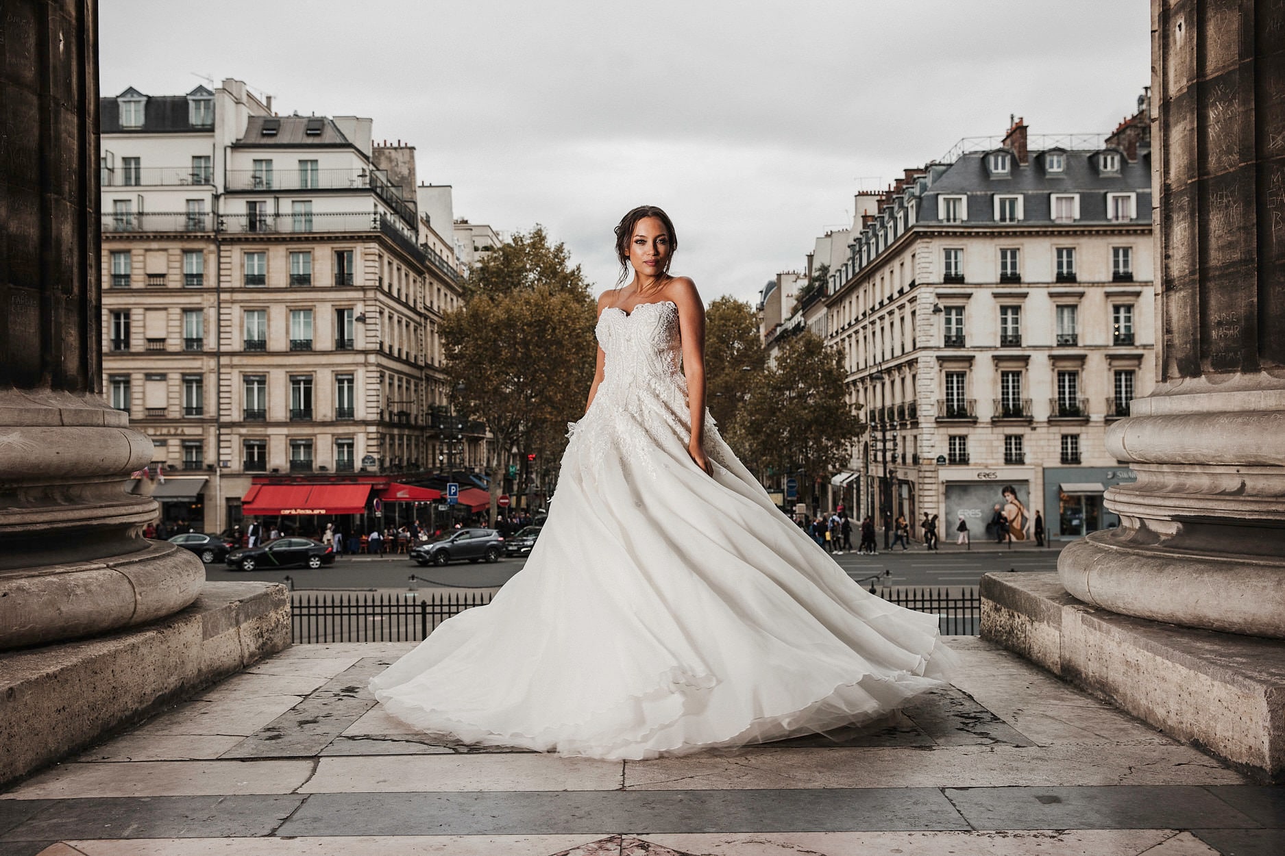 A bride on the steps of a monument, the Haussmann façades of the boulevard rising behind her