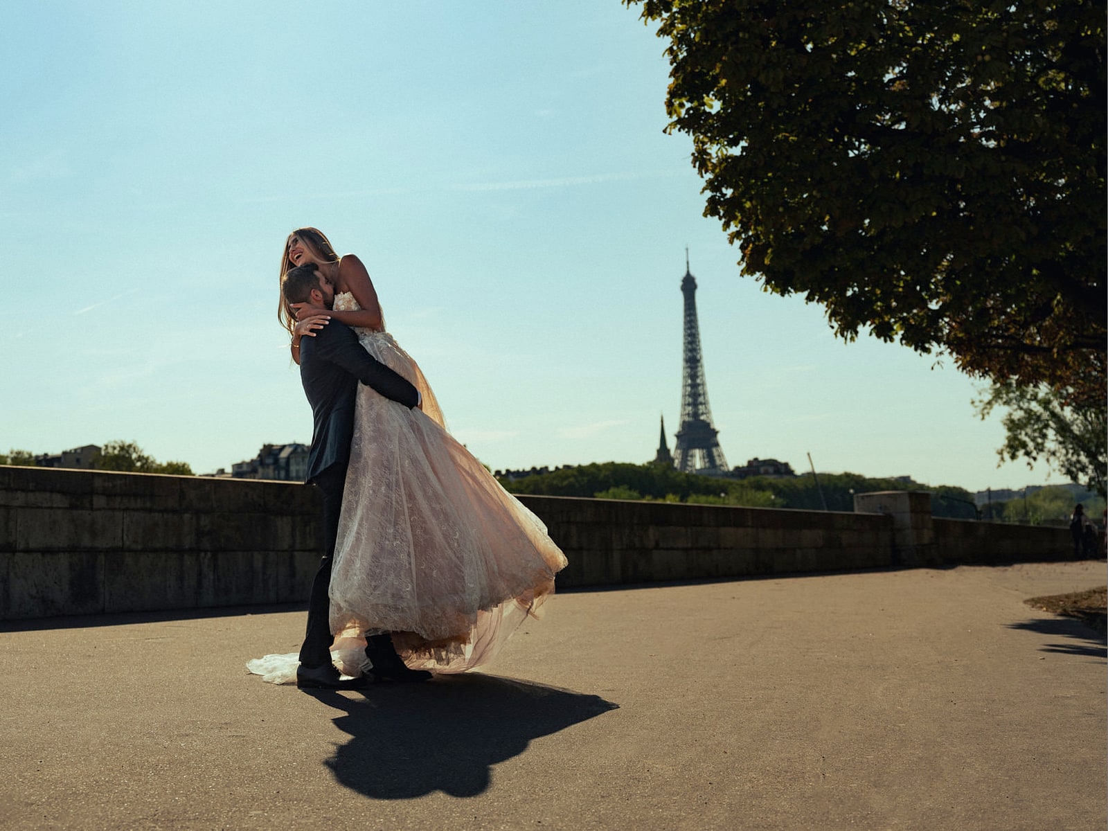 A groom turning his bride on the gravel of the Trocadéro gardens, the Eiffel Tower behind the trees