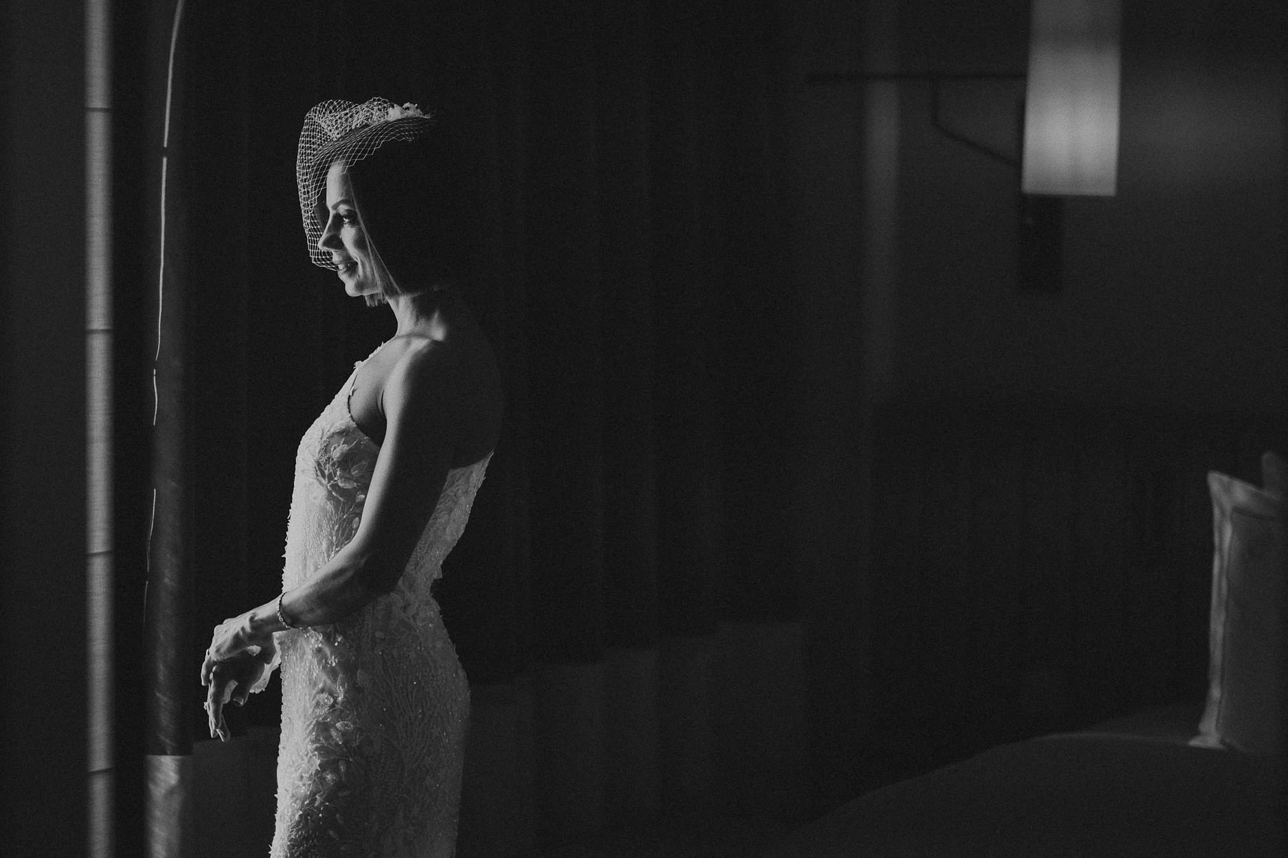 A bride standing in near darkness, only the beadwork of her dress catching any light