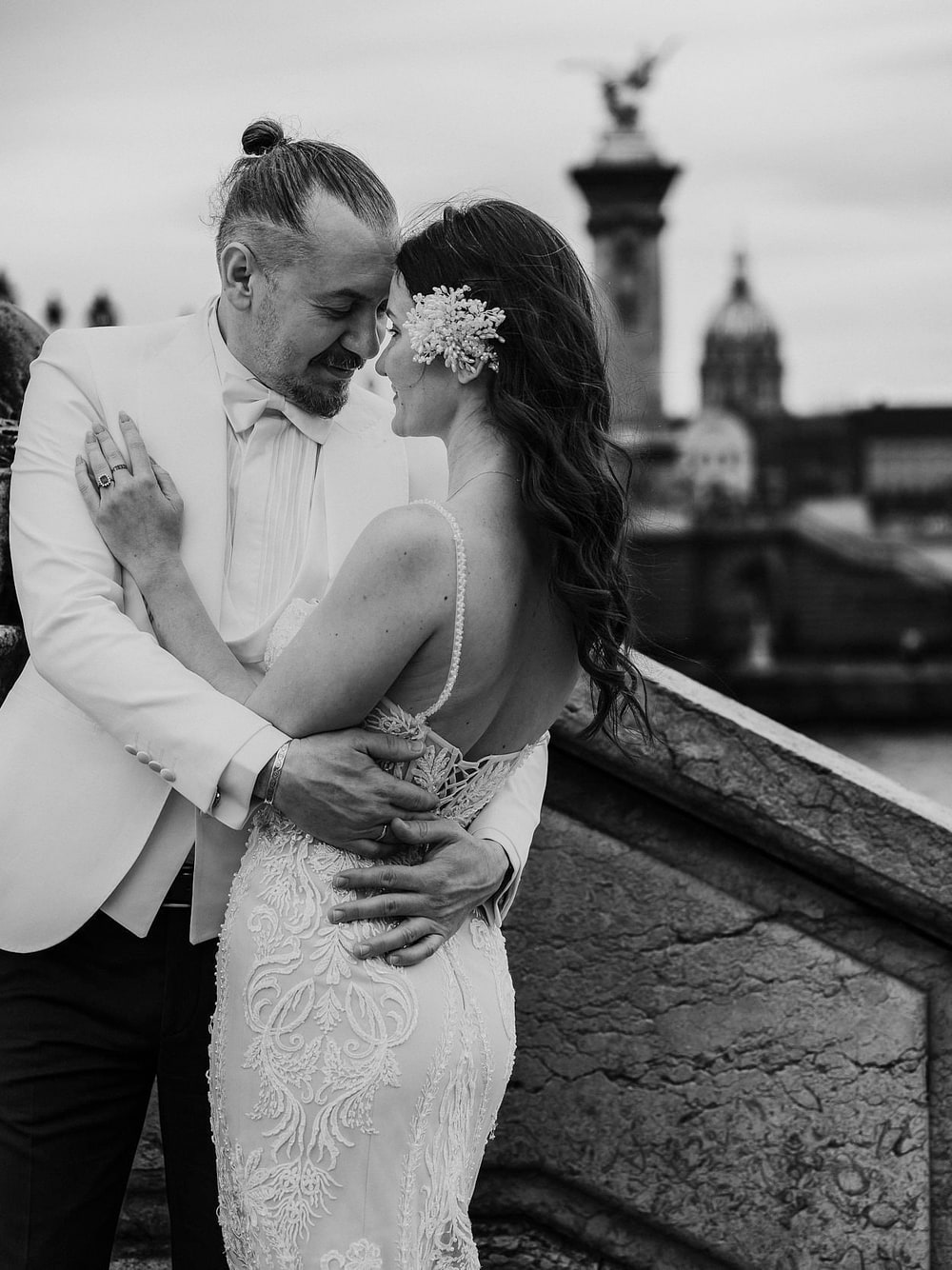 A couple leaning into one another at the rail of the Pont Alexandre III in black and white