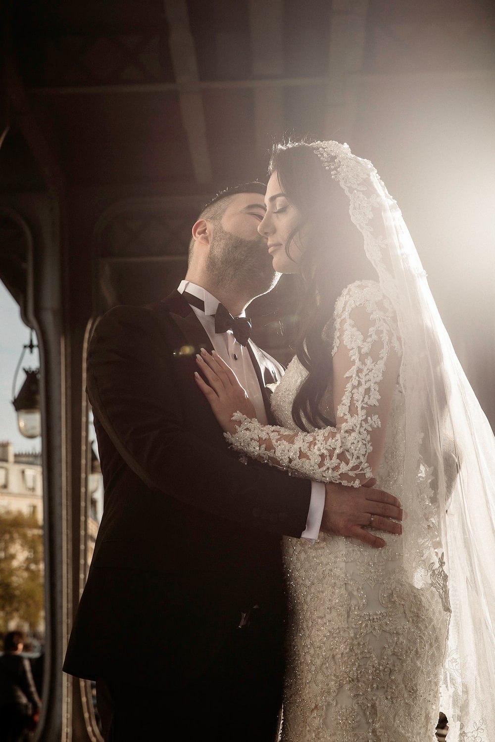 A couple standing forehead to forehead beneath a veil, lit from behind by a doorway