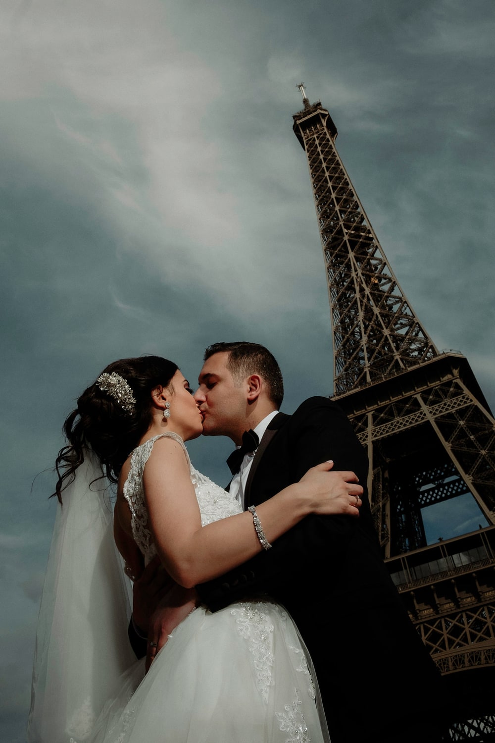 A couple kissing directly beneath the Eiffel Tower under a stormy sky
