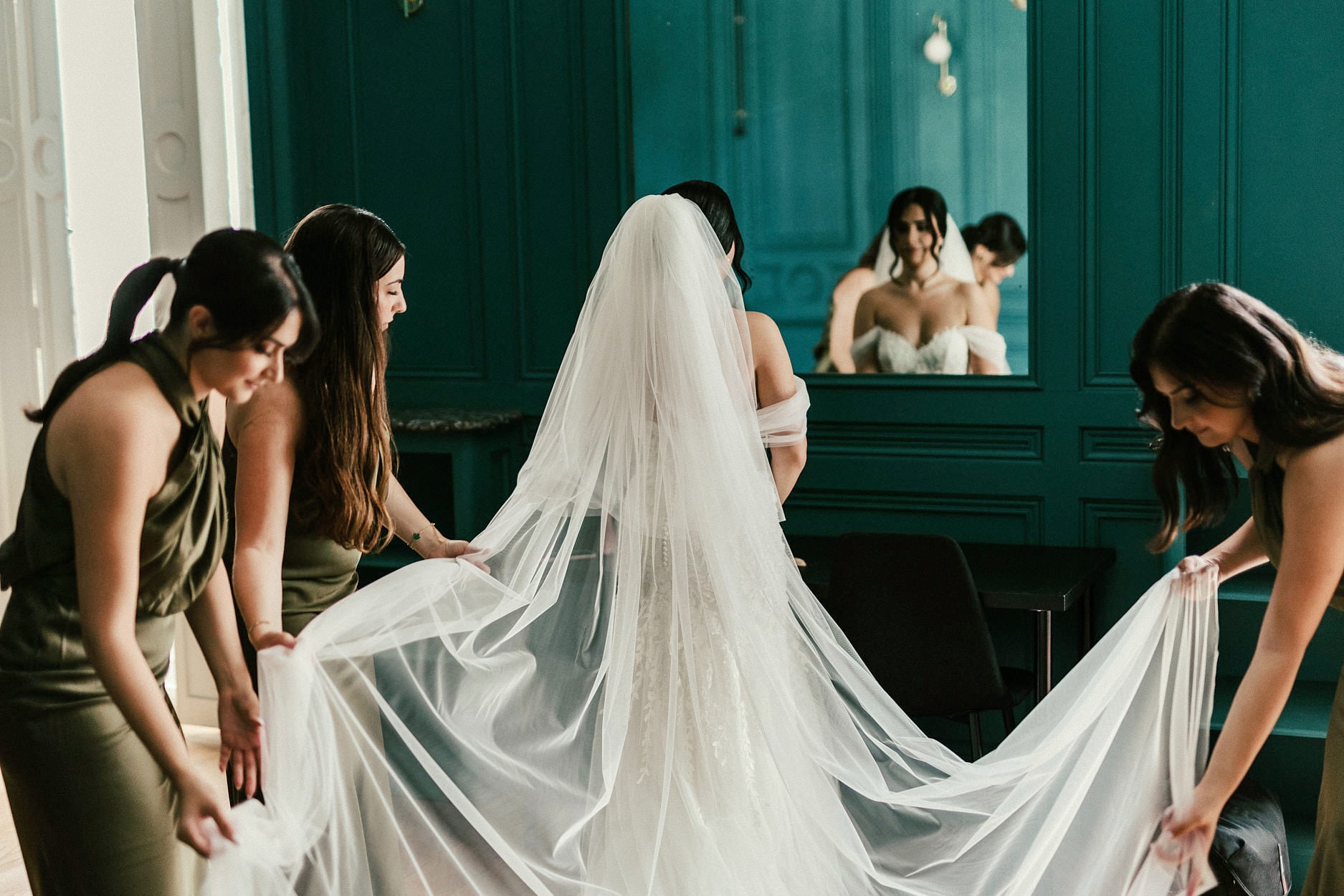 Bridesmaids carrying a bride’s veil out through a green painted door