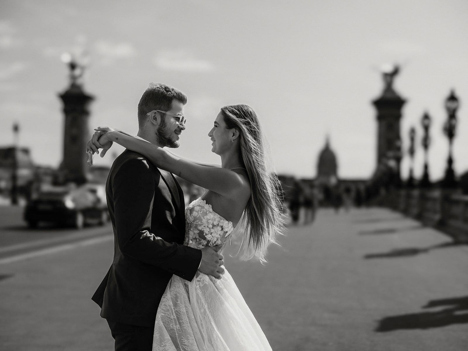 A bride and groom leaning into each other in the middle of the Pont Alexandre III, the Invalides dome behind