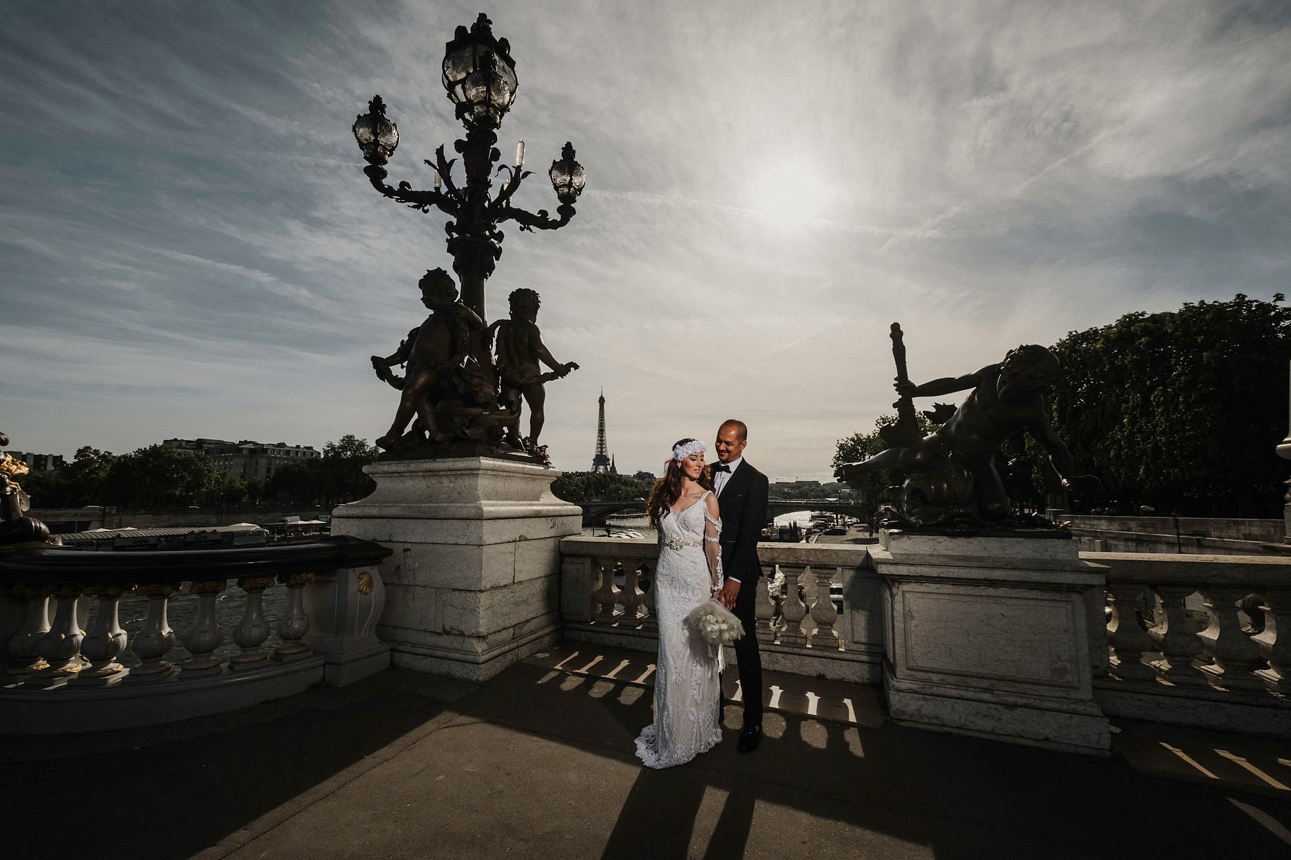 A bride and groom on the Pont Alexandre III at dusk, the statues and lamps of the bridge above them