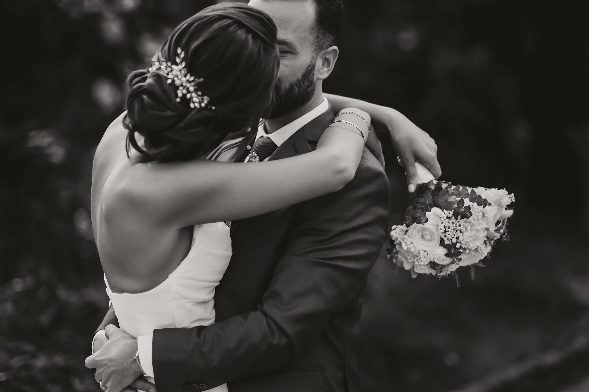 A bride with both arms around her husband’s neck, bouquet still in her hand