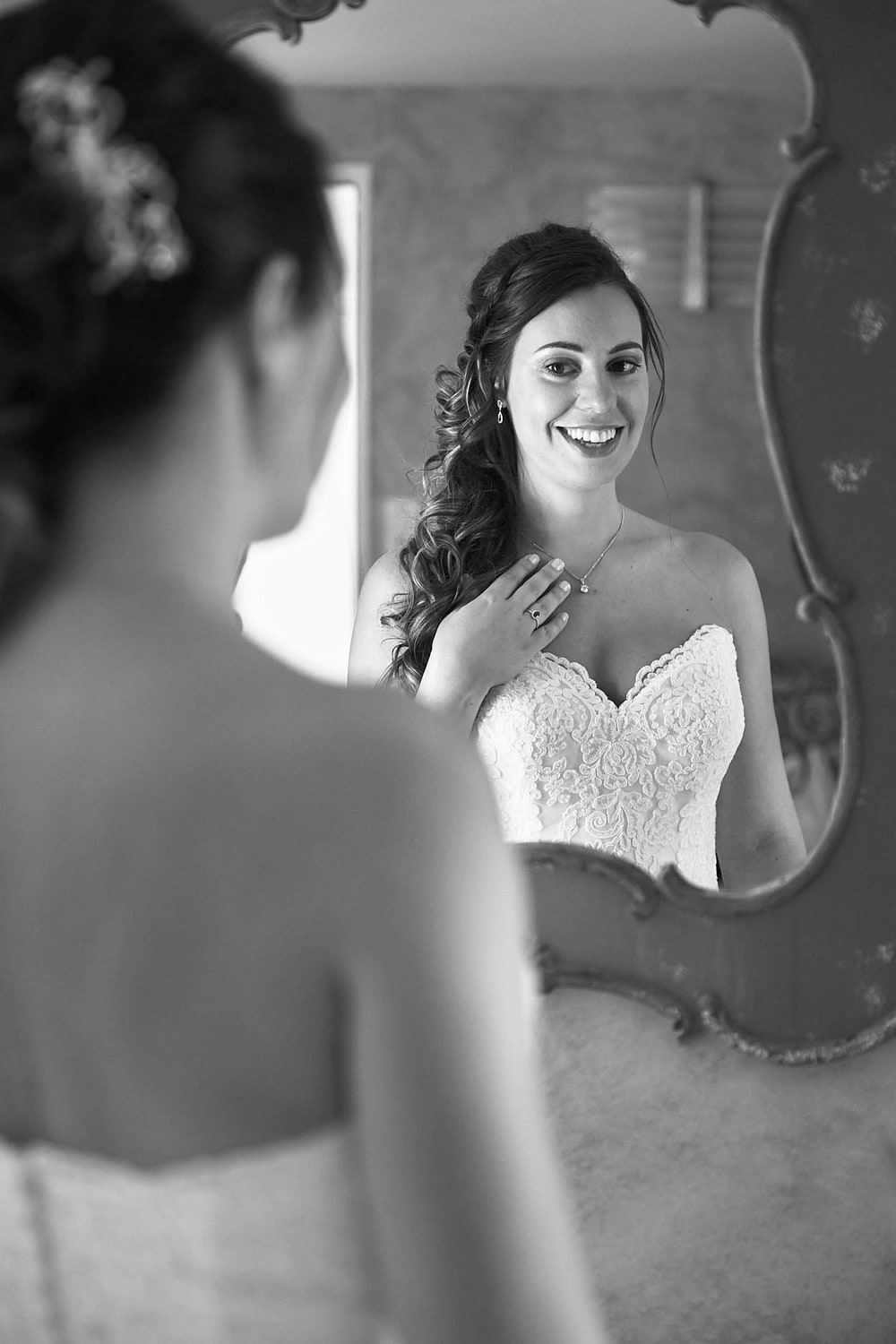 A bride smiling at her reflection in a tall mirror