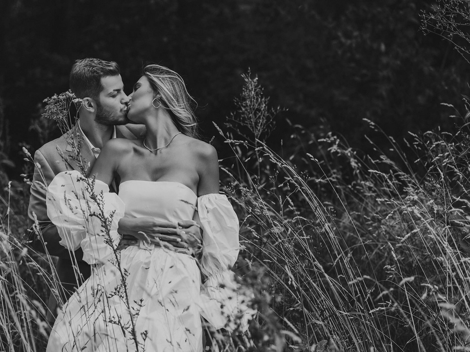 A couple kissing in waist-high summer grass, photographed through the seed heads
