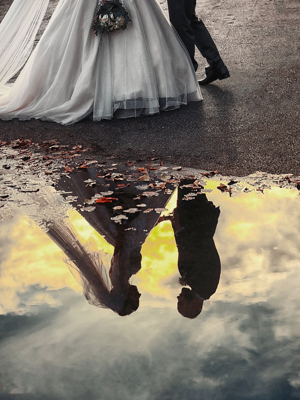 A bride and groom seen upside down in the reflection of a rain puddle on a Paris pavement