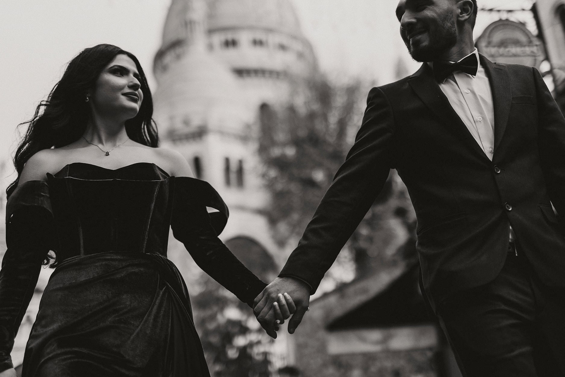A couple in black evening dress walking hand in hand down the steps below the Sacré-Cœur, photographed from low down