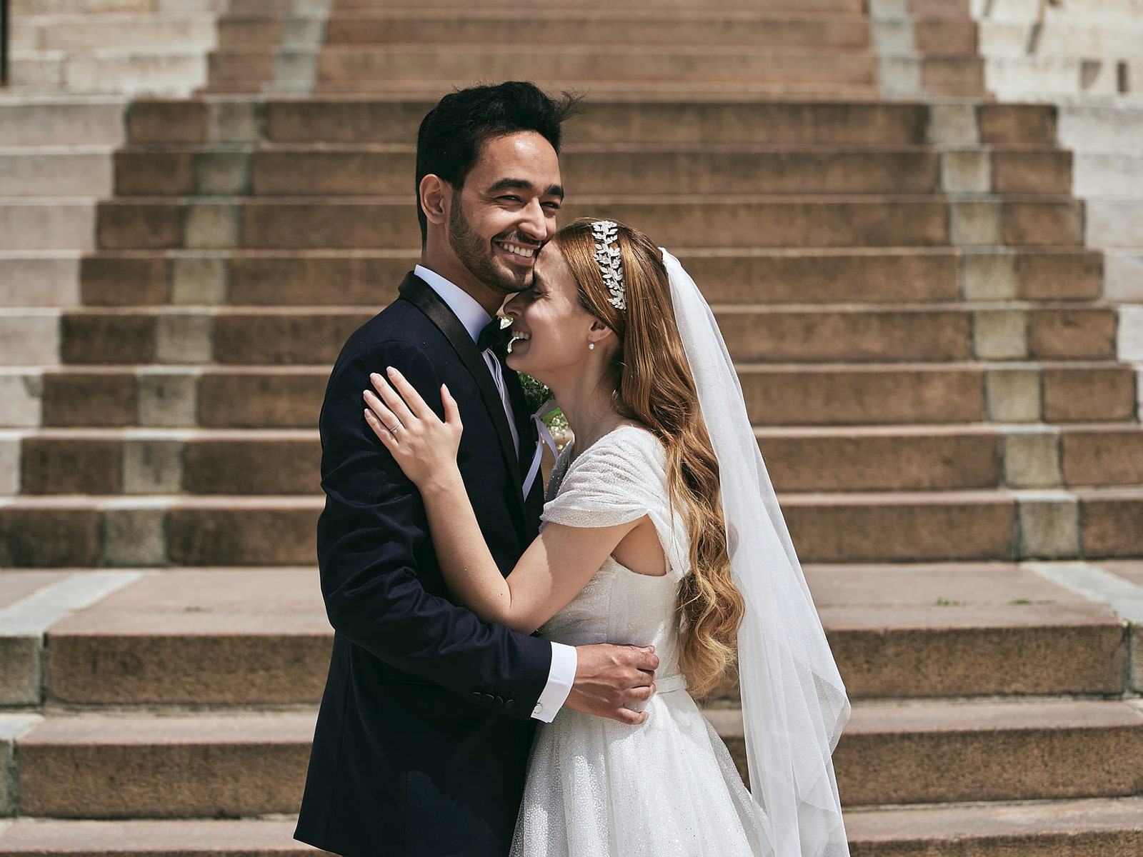A bride and groom close together on a flight of pale stone steps