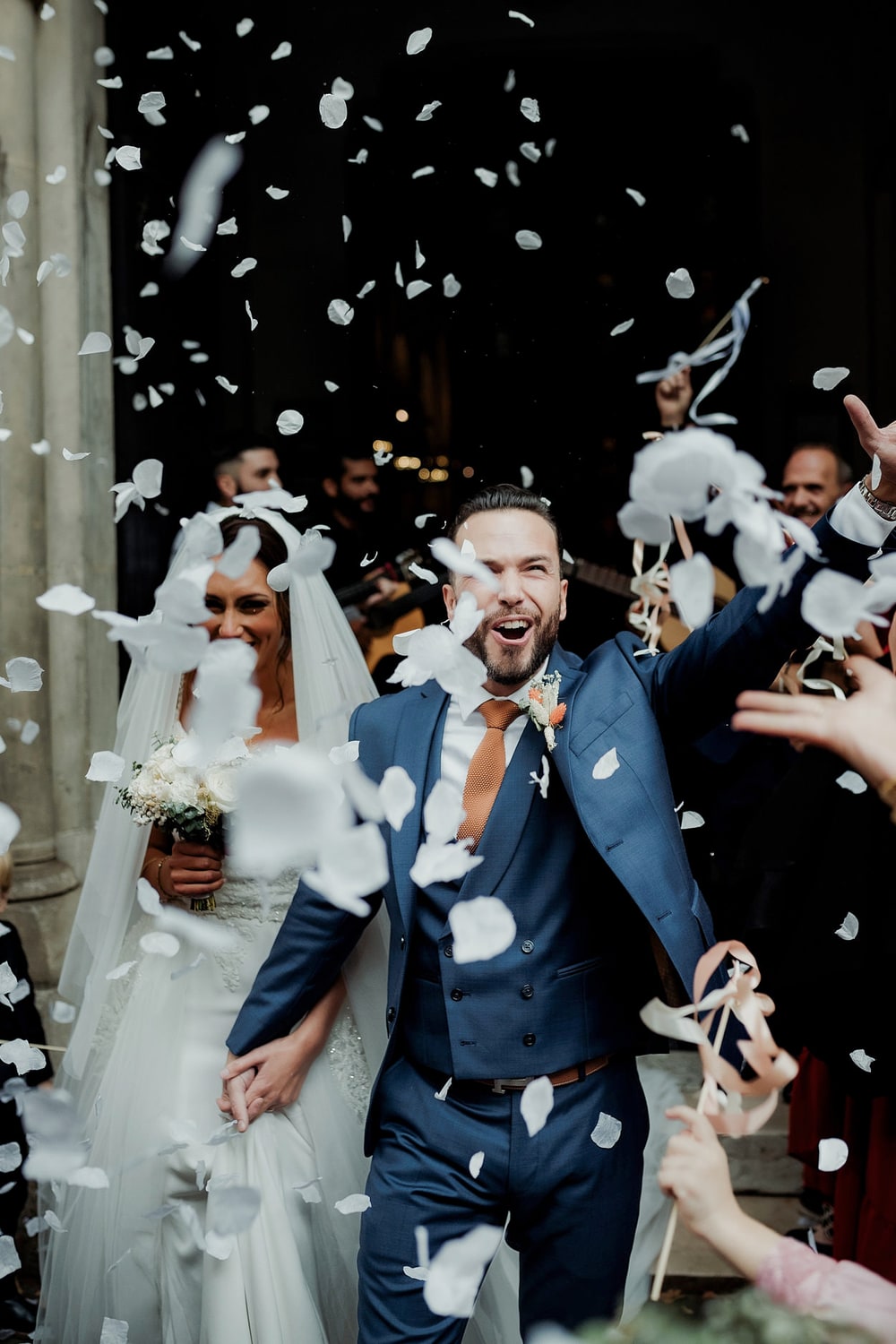 A couple stepping out into a storm of white confetti, both laughing