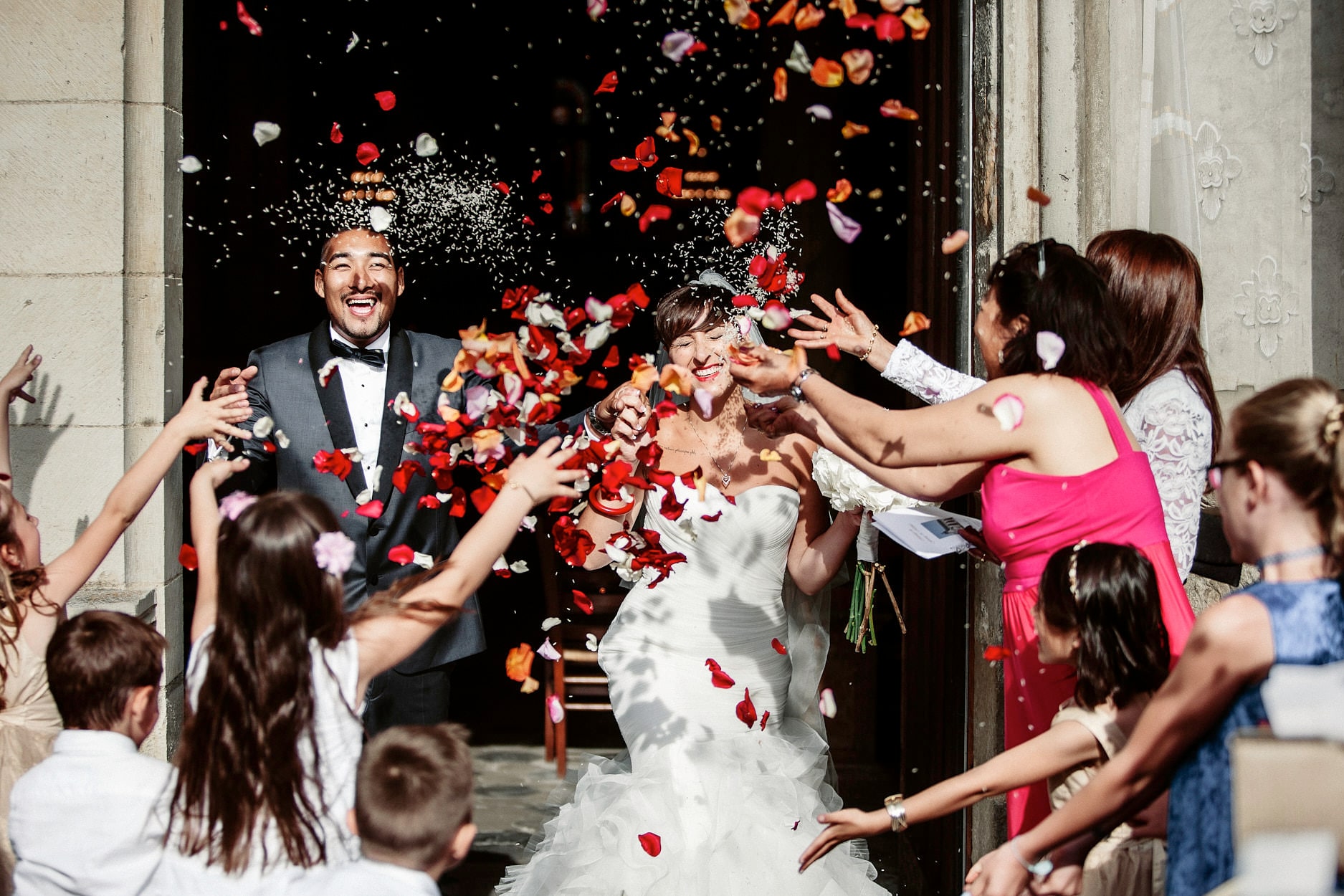 Guests throwing red and orange petals over a couple in a doorway