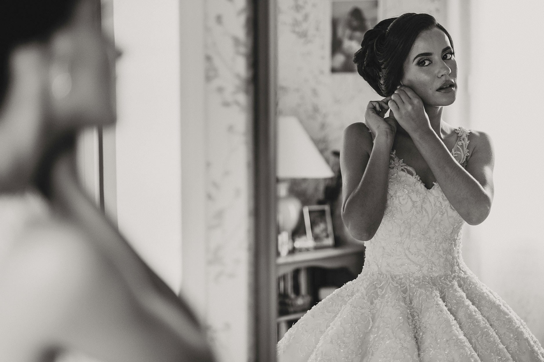 A bride fastening an earring at a doorway, framed by the room beyond