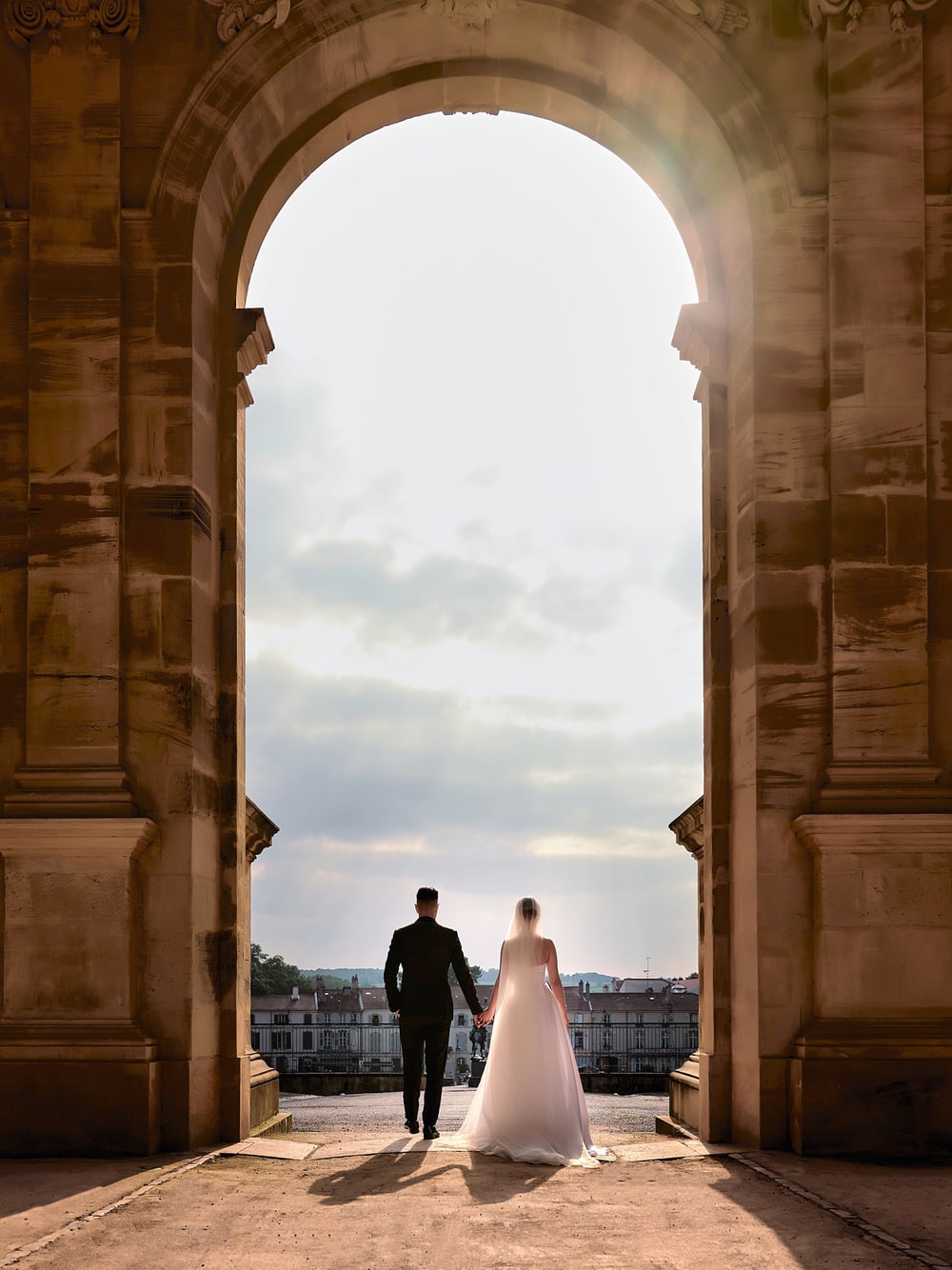 A couple standing at the far side of a great stone arch, looking out over the rooftops