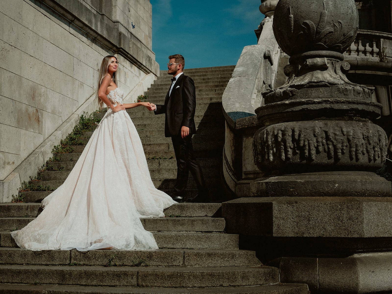 A bride and groom on a carved stone staircase, her train falling down the steps