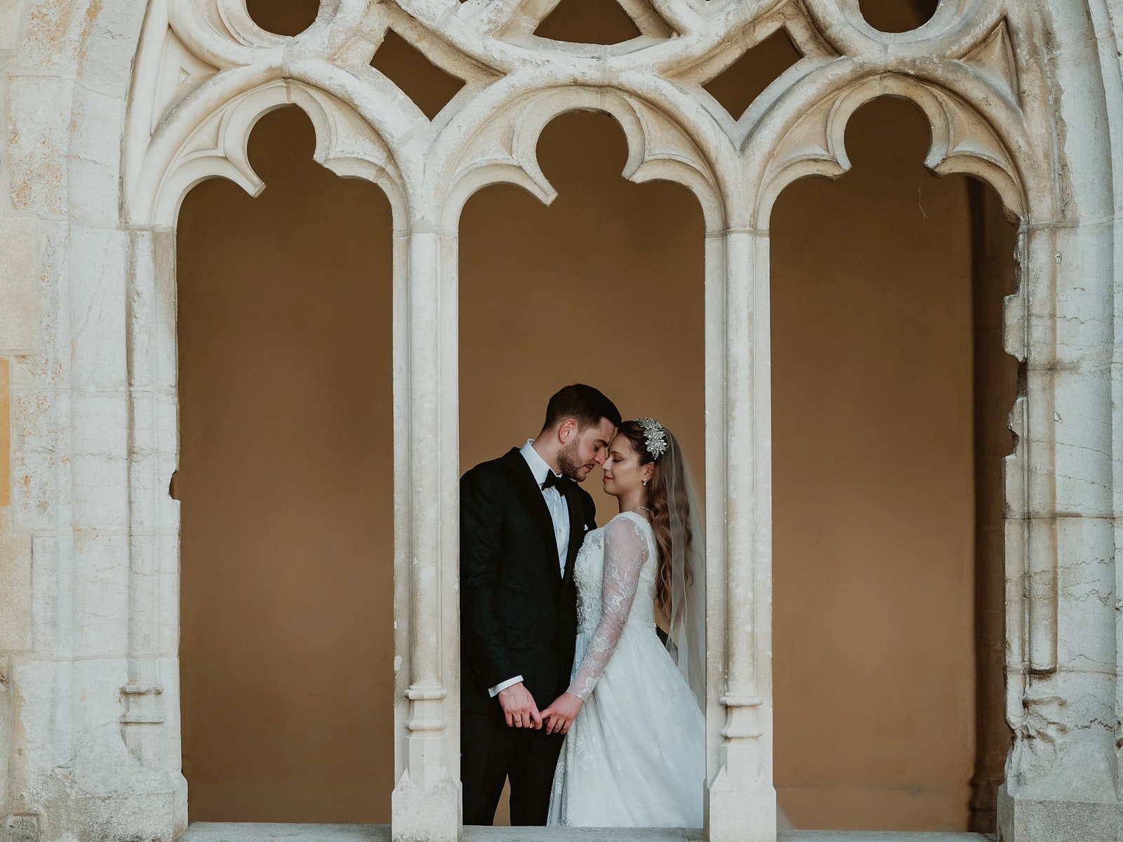 A couple standing quietly inside the traceried window of an old cloister