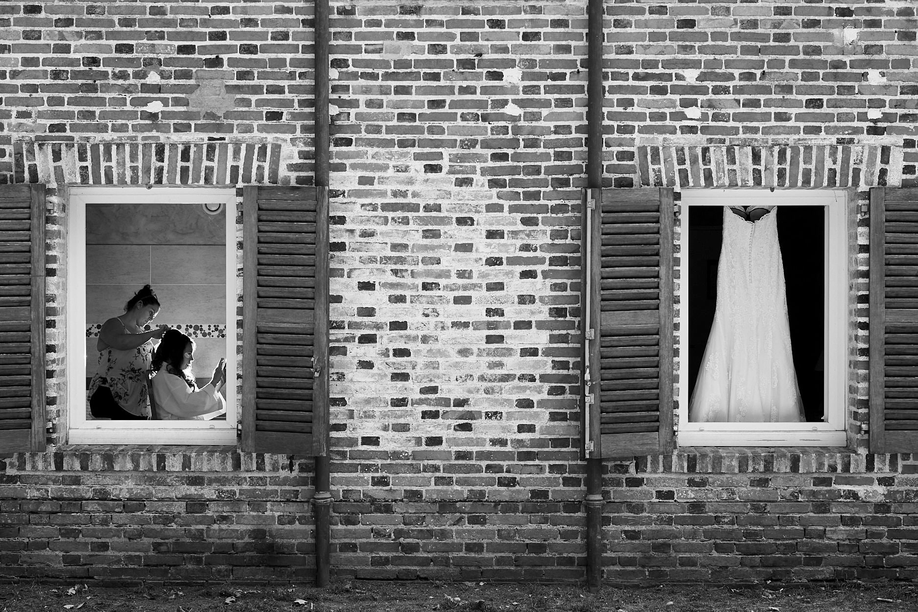 A brick wall with two windows: a wedding dress hanging in one, a couple reflected in the other