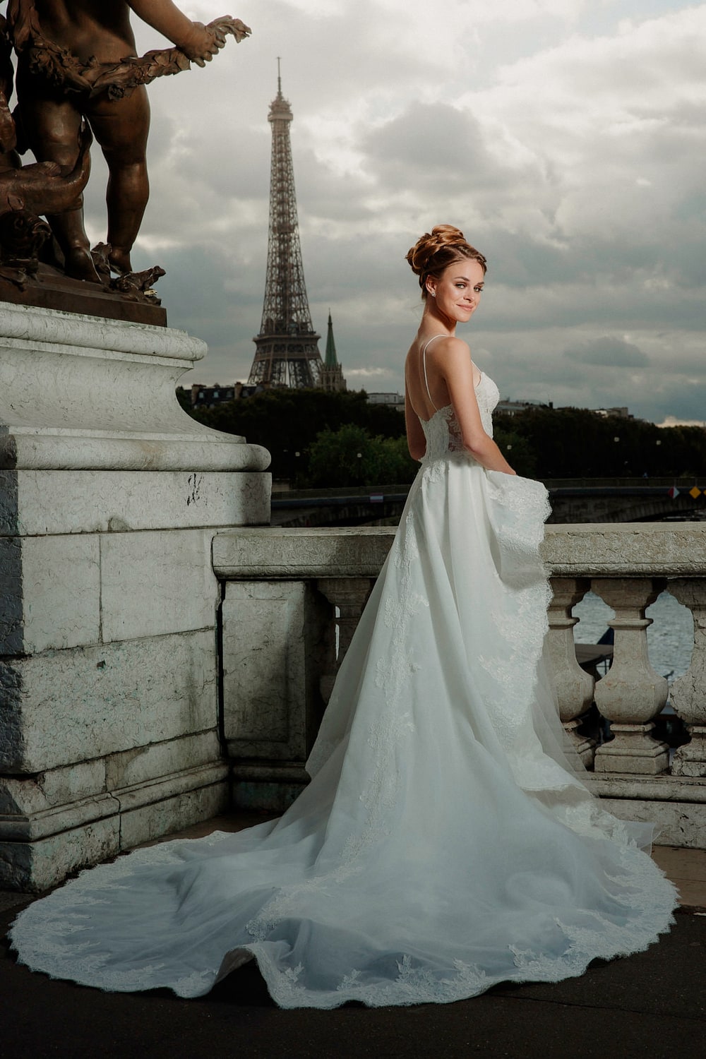 A bride gathering her train beside a gilded statue, the Eiffel Tower framed behind