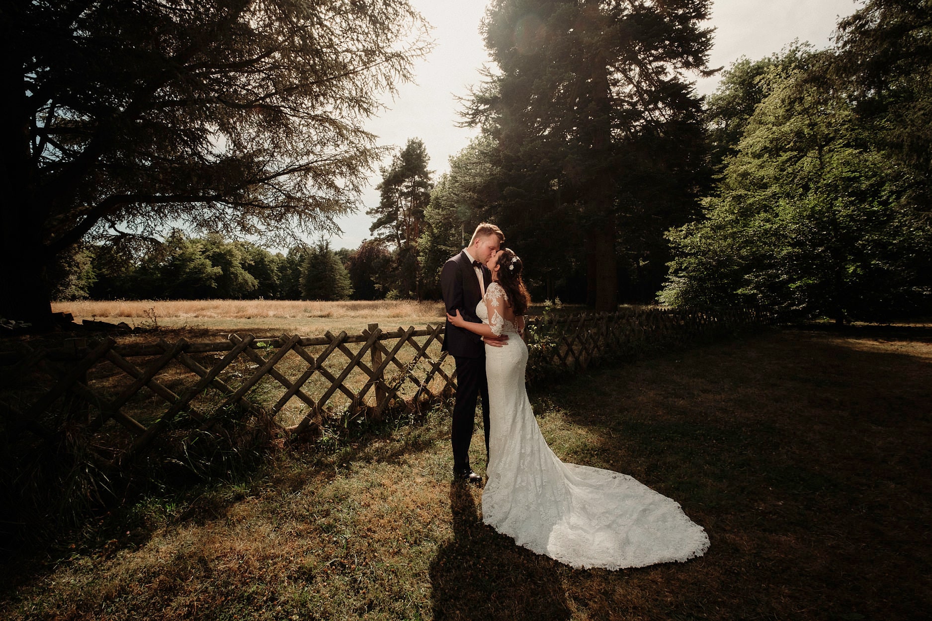 A couple standing at the edge of a park as the sun drops behind the trees