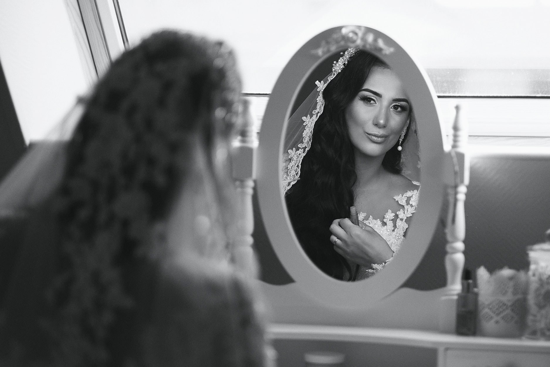 A bride looking at herself in an oval mirror while her hair is finished