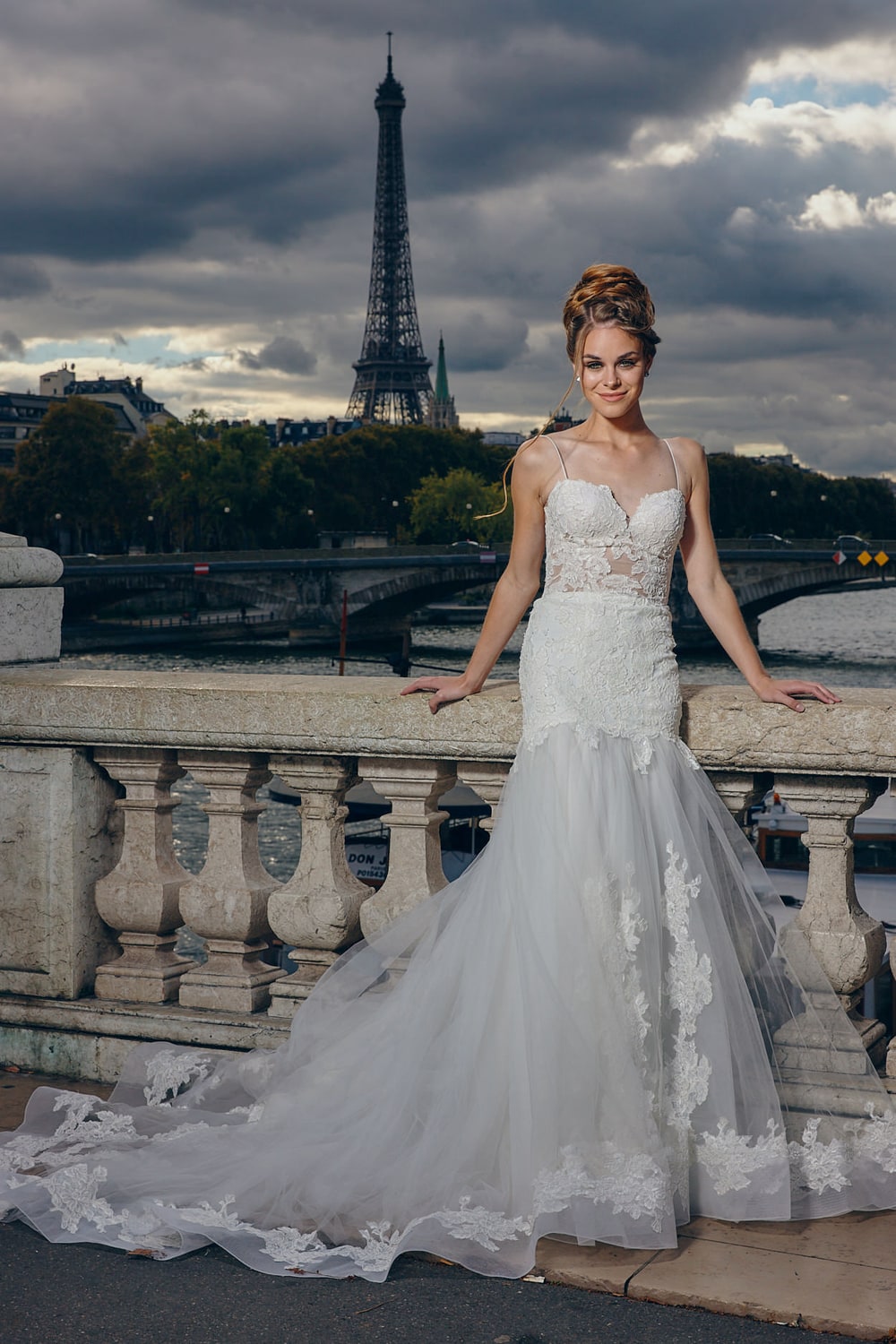 A bride resting against a stone balustrade above the Seine with the Eiffel Tower behind her