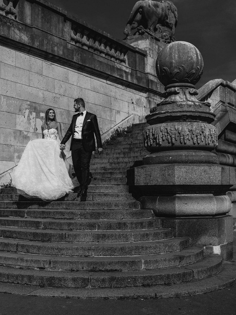 A bride and groom climbing a monumental stone staircase, small against the carved stonework