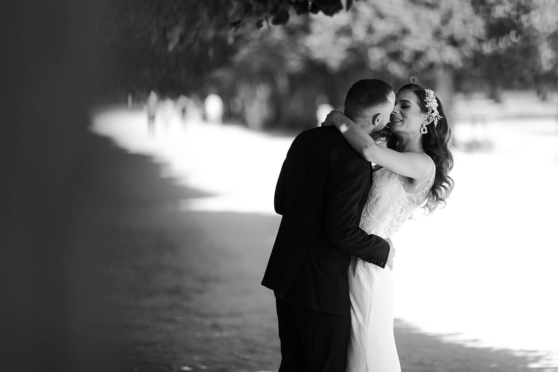 A couple laughing in an embrace under a line of plane trees, the path behind them burnt out to white