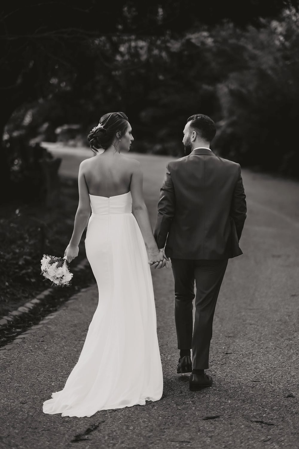 A bride and groom walking away down an empty road, photographed from behind in black and white
