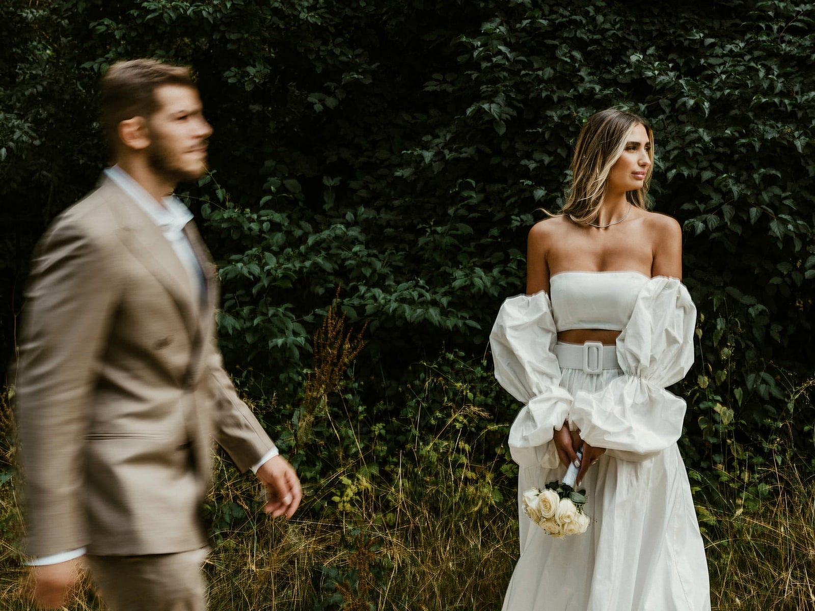 A couple walking apart from each other into deep green undergrowth, mid-step