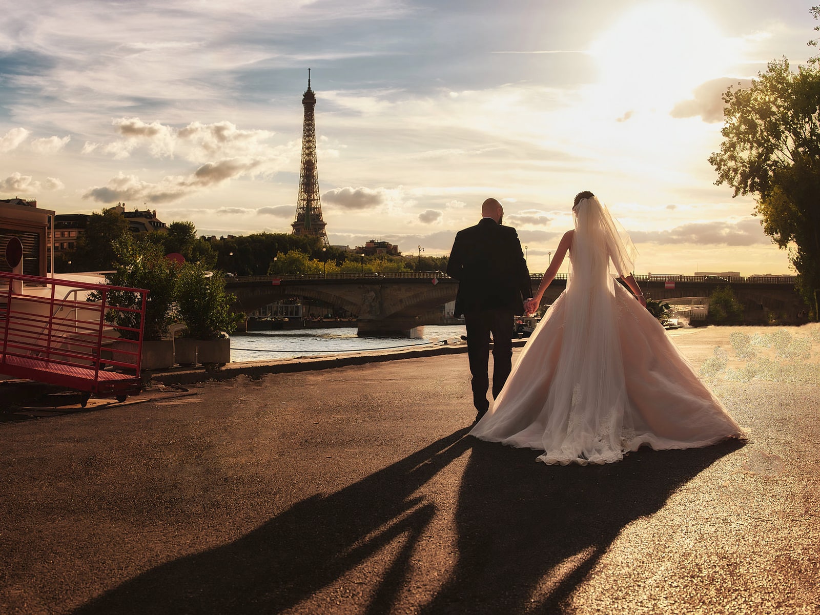 A bride and groom walking away along the Seine at sunset, their shadows stretching ahead of them and the Eiffel Tower catching the last light